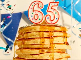 A stack of pancakes with "65" birthday candles. 